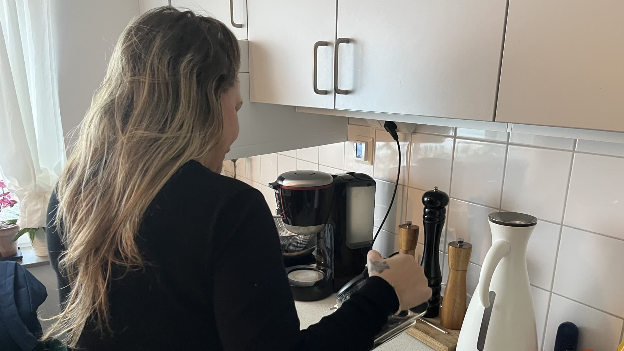 Fyrabarnsmamman Veronica står i ett kök med ryggen mot kameran. Hon håller i en svart sladd och är omgiven av köksredskap som kaffemaskin, vattenkokare och kryddkvarnar.