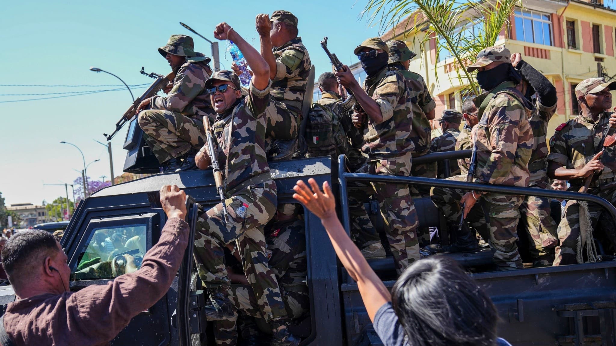 Soldater i kamouflageuniformer står på ett militärfordon och hälsar på en samling människor som sträcker upp händerna under en ceremoni för att hedra demonstranter som dödats i Antananarivo, Madagaskar.