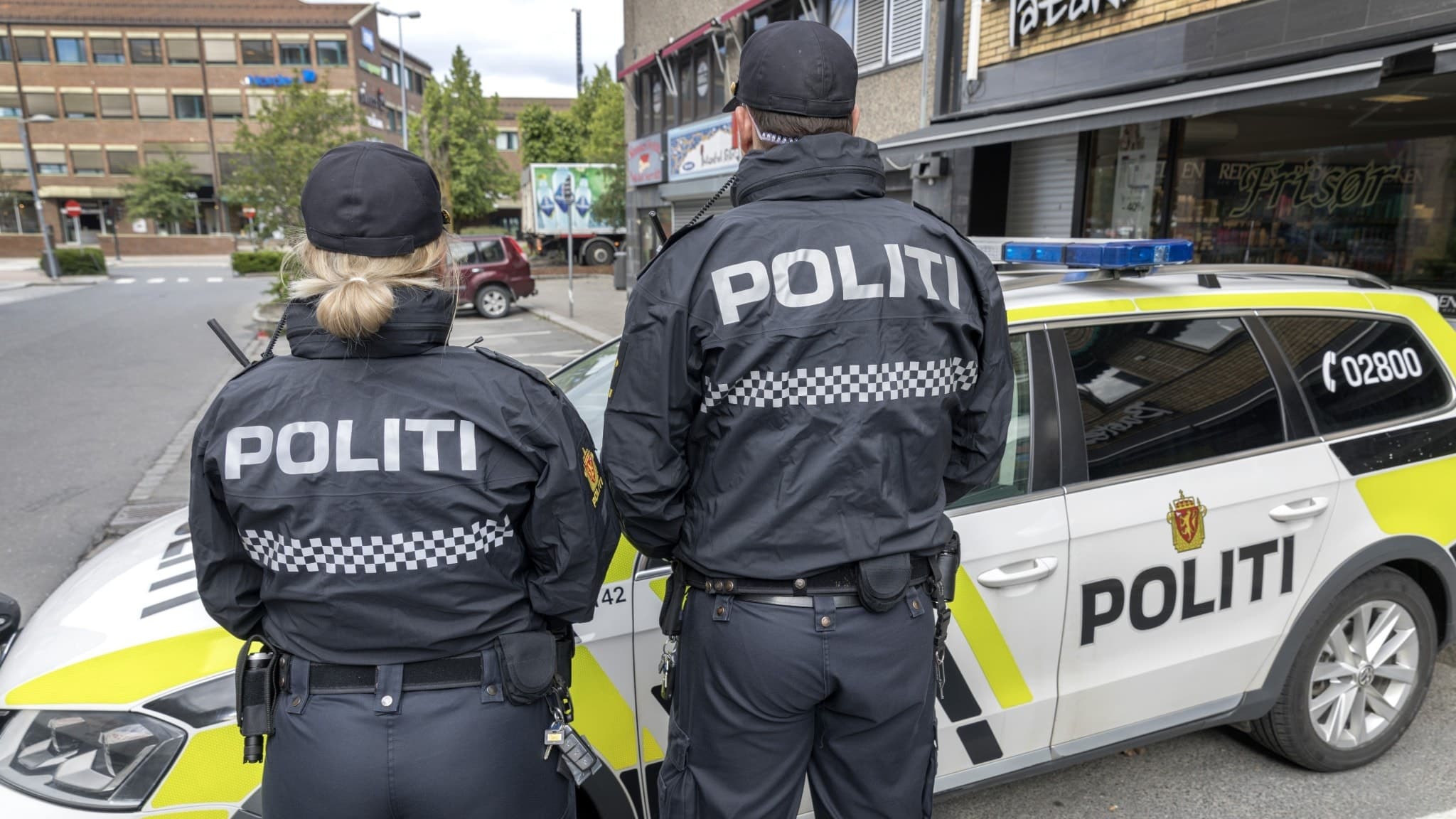 Två norska poliser bakifrån framför polisbil