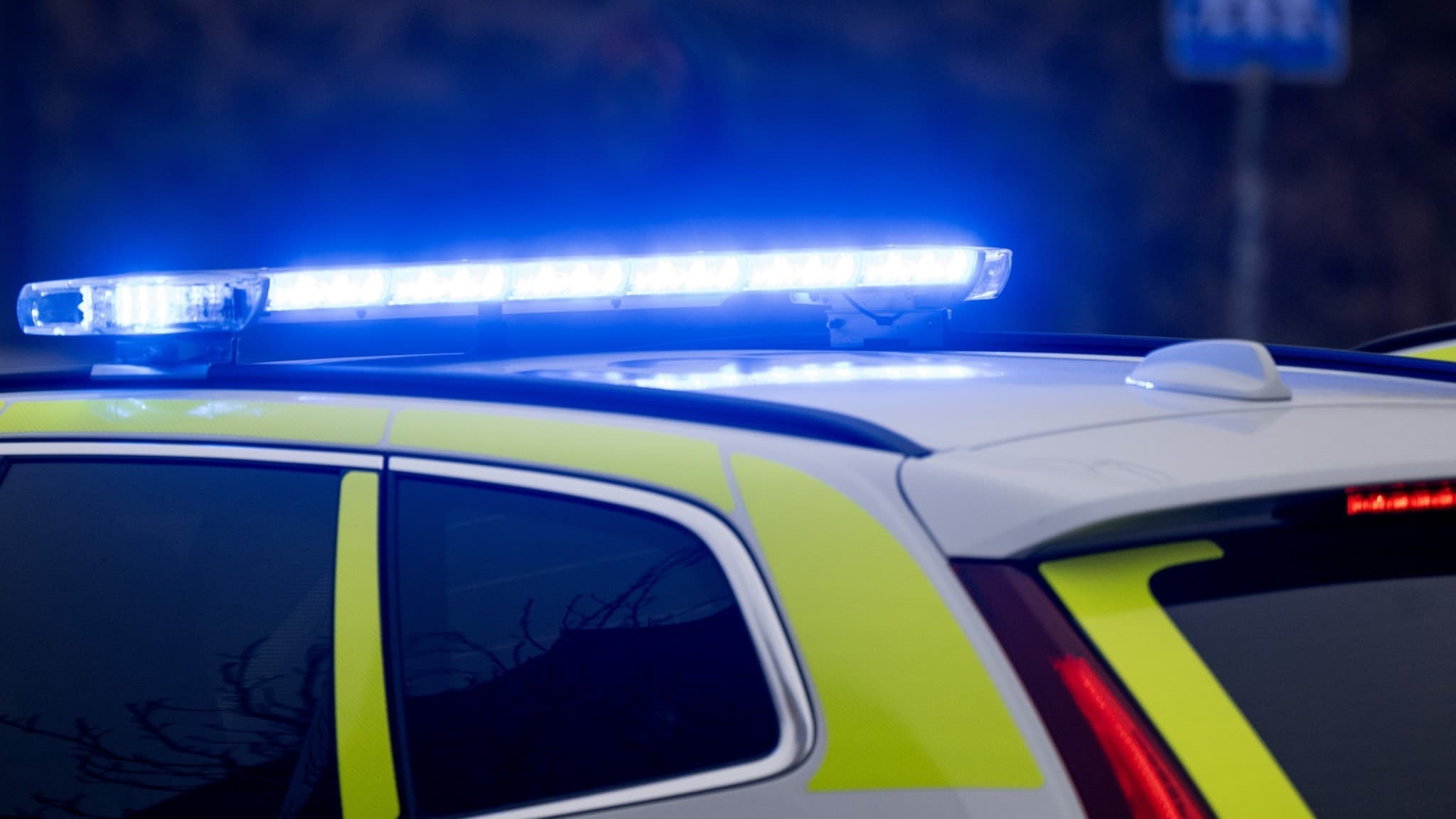 Polisbil med blåljus på taket, parkerad nära en övergångsskylt. Bilden symboliserar ett pågående polisärende där ett barn ska ha blivit hotat med kniv av en okänd gärningsman.