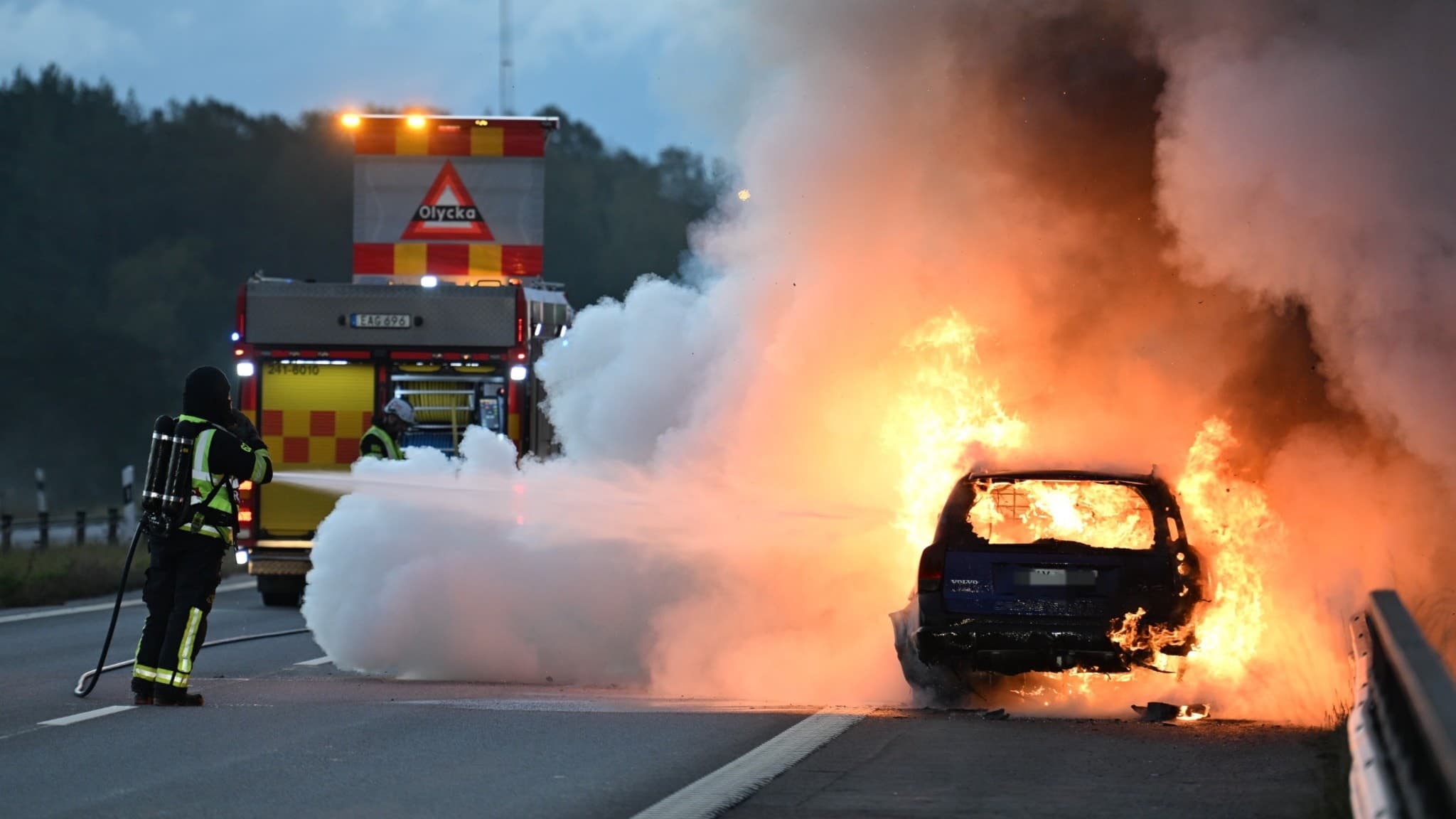 Bil brinner och räddningstjänsten sprutar vatten.