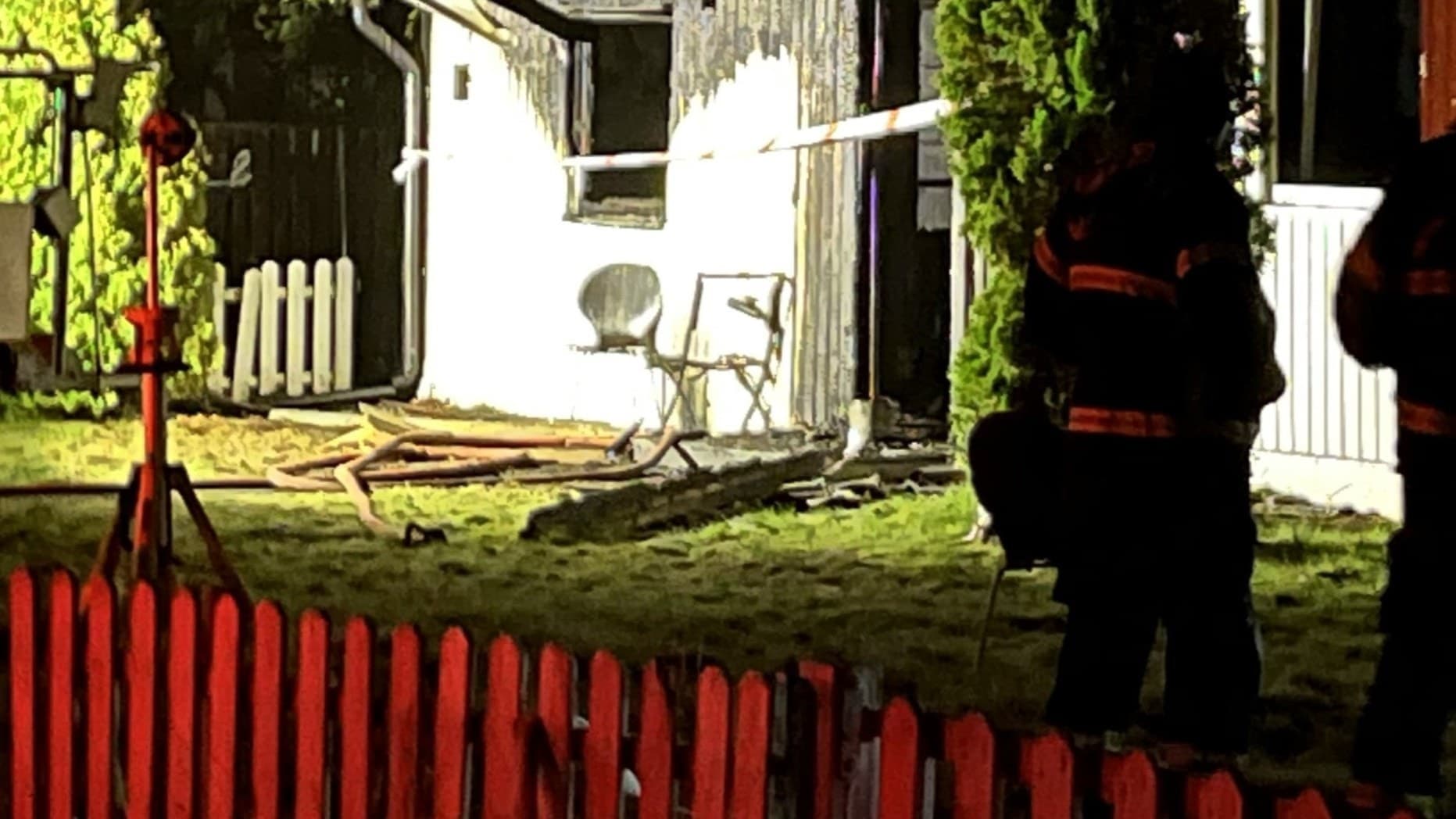 Brandmän arbetar vid en villabrand där fasaden är skadad och bränt trä syns.