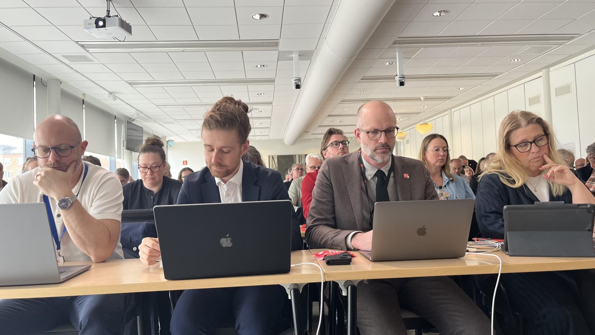 Foto från möte där fyra personer sitter bredvid varandra med dator och surfplatta framför sig.