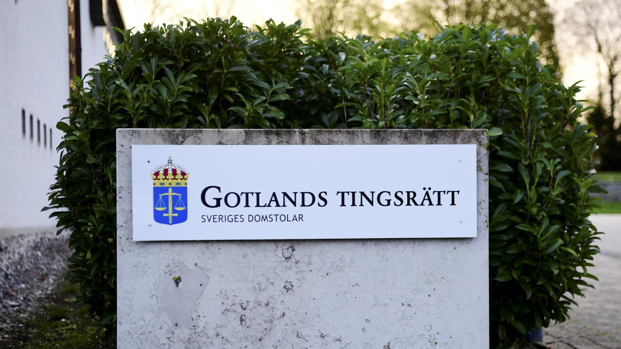 Entréskylt med texten 'Gotlands tingsrätt' framför grön buske. Tingsrätten är aktuell i samband med en rättegång om terroristbrott i Visby.