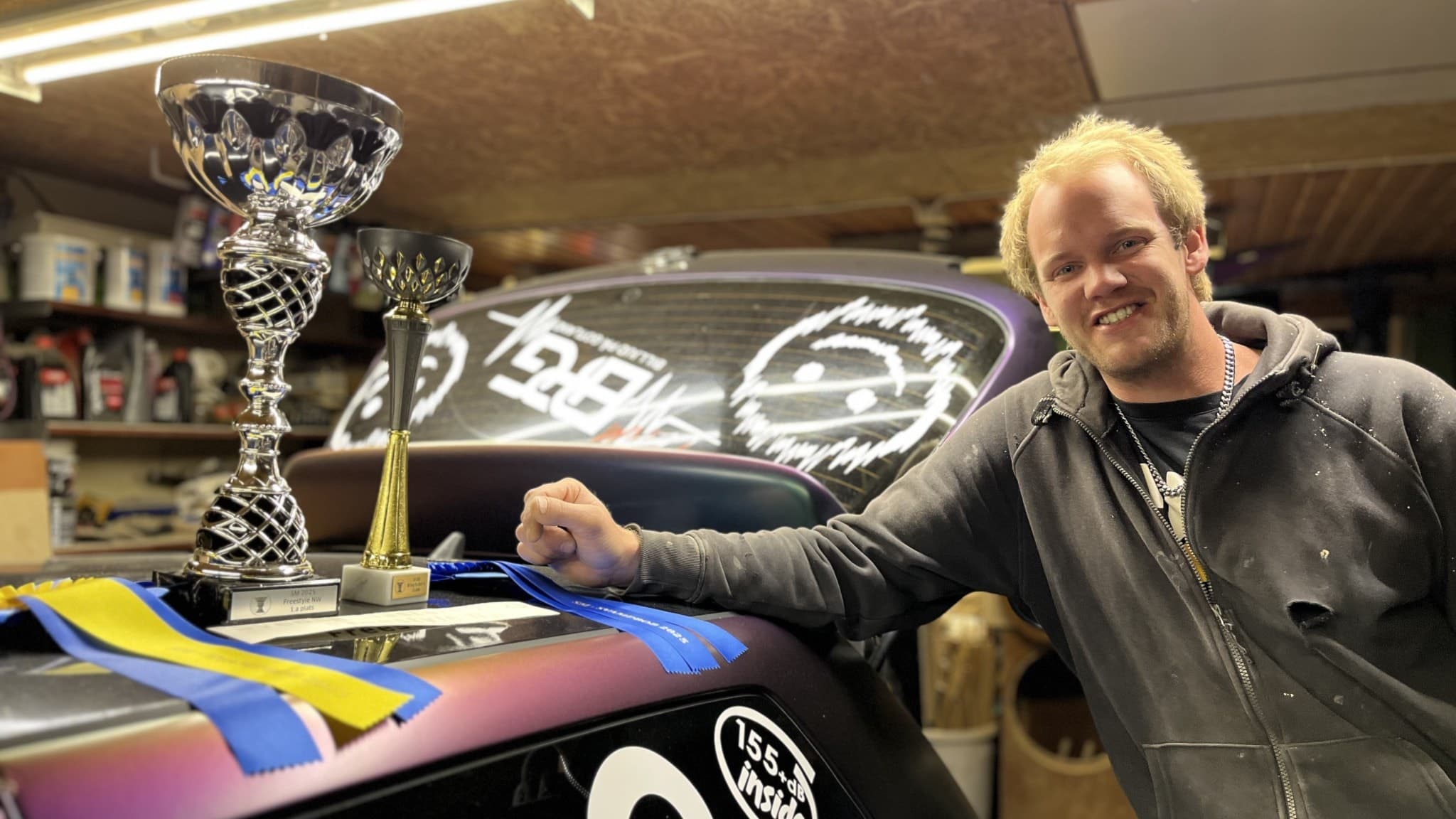 Robert Hamberg står bredvid en bil med pokaler på huven. 