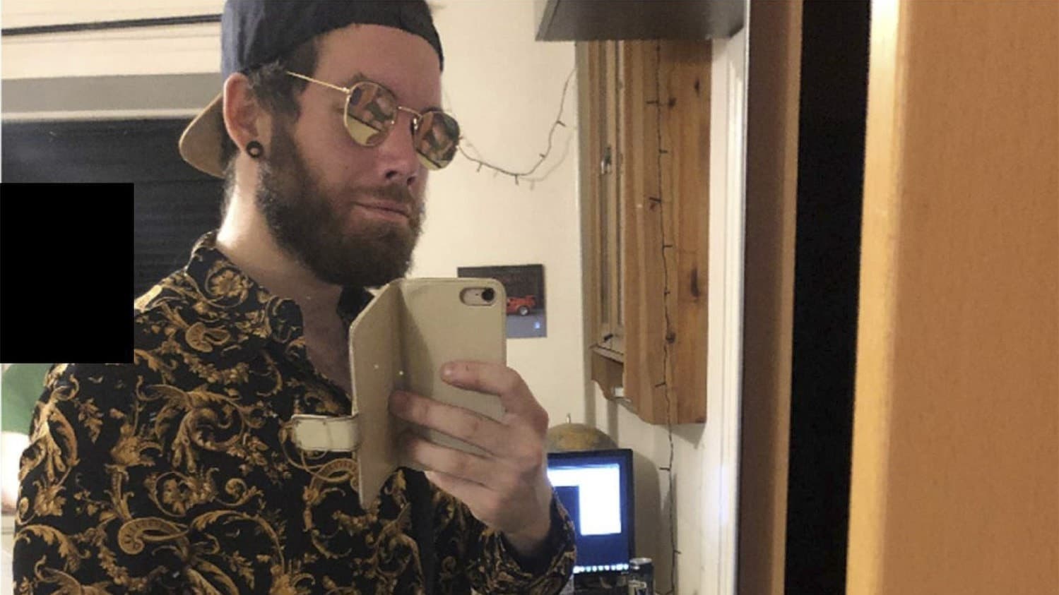 En person i mönstrad skjorta och keps tar en selfie i ett rum där en dator och skrivbord syns i bakgrunden. Bilden är relaterad till förundersökningen av Nytorgsmannen Fredrik Lundgren.