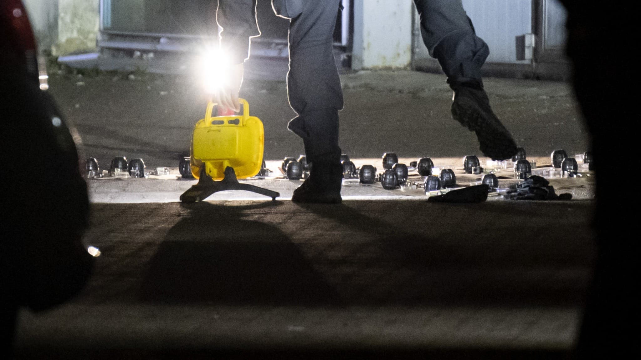 Bombtekniker arbetar vid avspärrat industriområde utanför Malmö där flera handgranater har hittats. Flera föremål ligger uppradade på marken under stark belysning.