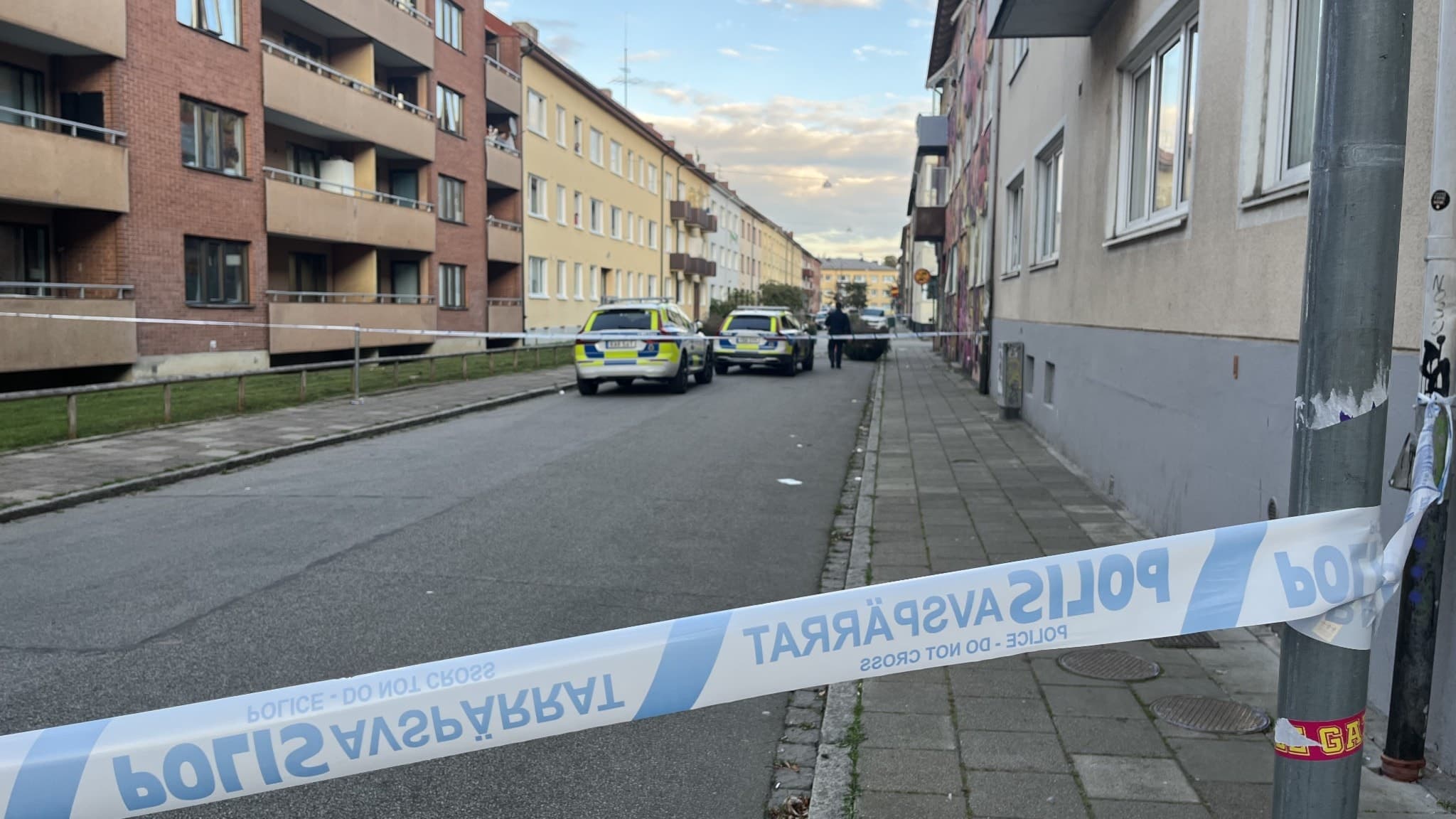 Avspärrad gata i ett bostadsområde med flerfamiljshus i Malmö. Två polisfordon står parkerade vid trottoaren, och polistejp markerar avspärrningen.