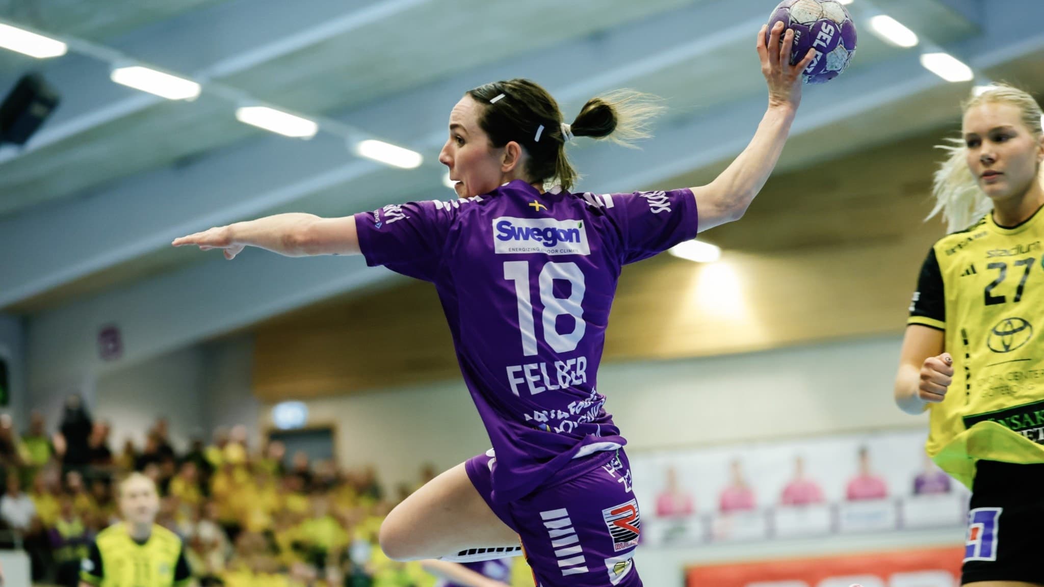 Skaras Melanie Felber i lila matchställ syns hoppa med bollen i höger hand och förbereder ett skott under en SM-final i handboll mot IK Sävehof i Skara idrottshall.