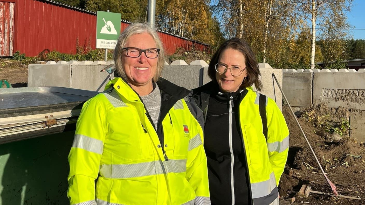 Två personer, Ulrica Jonsson och Maria Nyström, står utomhus i arbetskläder med reflexer framför en återvinningsstation med betongblock och en grön container i bakgrunden.