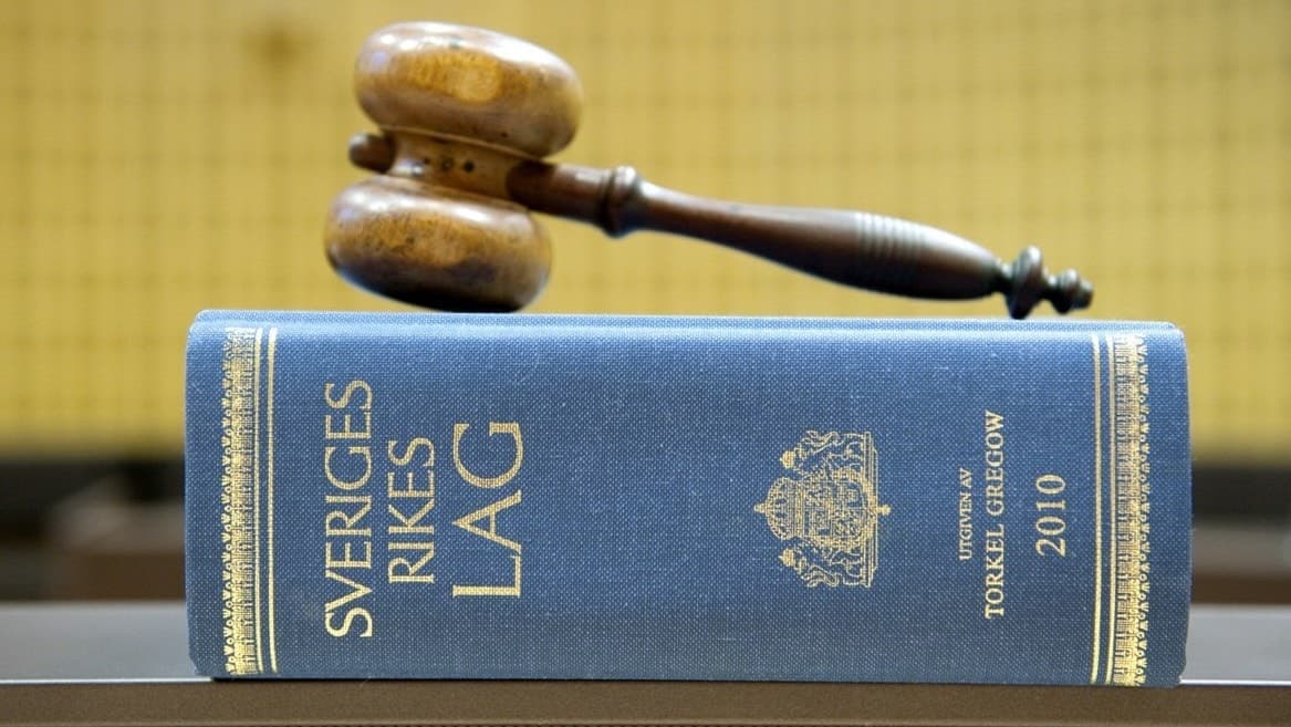 En domarklubba ligger ovanpå en lagbok med texten 'Sveriges Rikes lag'. Symbol för rättsväsendet och juridiska beslut i Sverige.