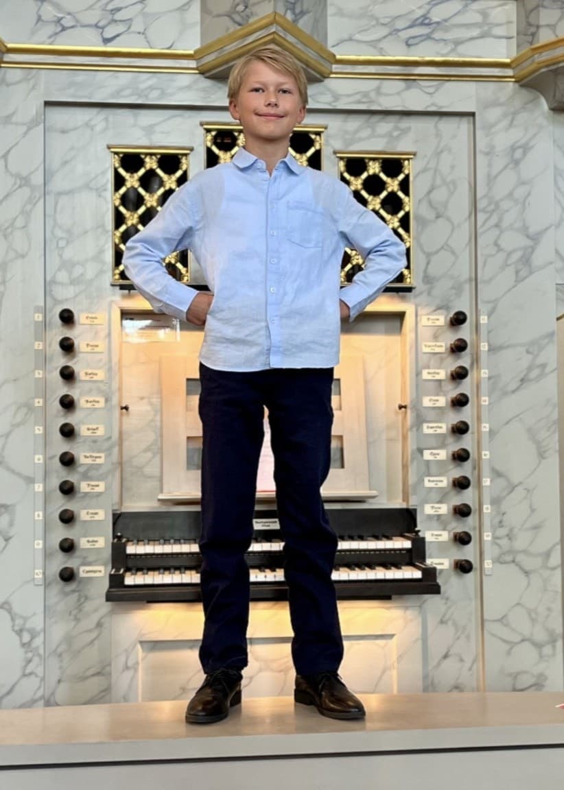Leon Löfgren, 9 år, står på en stor kyrkorgel med händerna på höfterna. Han bär en ljusblå skjorta och mörka byxor, och ser målmedveten ut. Bilden är tagen inne i en kyrka.