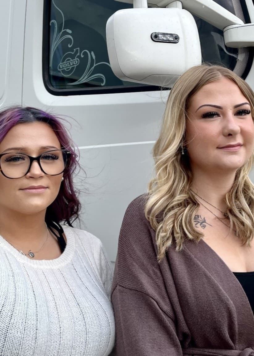 Två unga kvinnor, Tilda Hallberg och Celine Karlsson, står framför en vit lastbil. De går Fordons- och transportprogrammet och representerar den växande andelen kvinnor inom lastbilsbranschen.