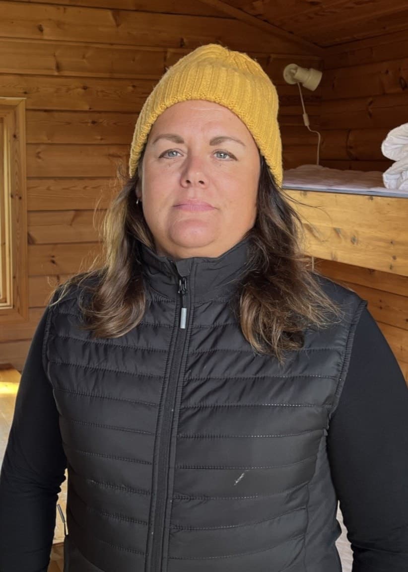 Kim Hedin, ordförande i Krokom Dvärsätts IF, står inne i en campingstuga med träväggar, våningssängar och ett fönster som vetter mot sjöutsikt.