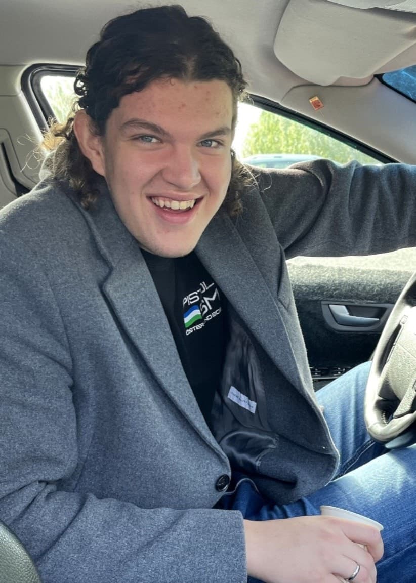 Max Wallin sitter i förarsätet på sin EPA-traktor i Östersund, klädd i grå kappa, med handen på ratten och solen skiner genom bilfönstret.