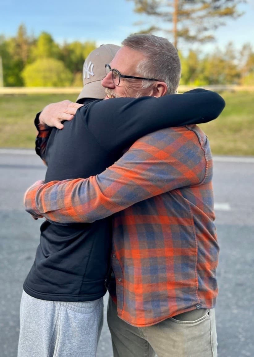 Isak Tellander och Ronny Johansson står på en landsväg omgiven av skog och grönska. Ena bilden visar en kram, den andra visar dem stående bredvid varandra med avslappnade leenden.