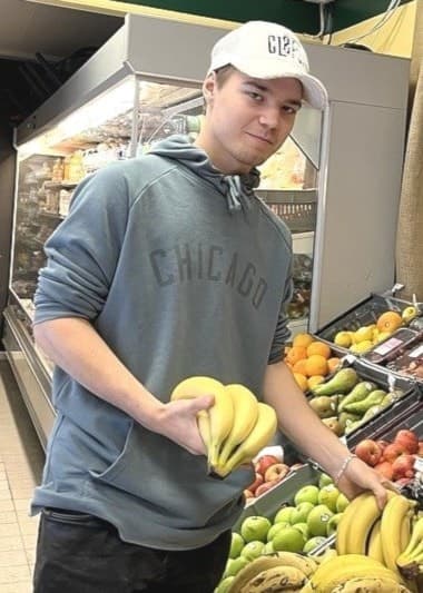 Nya butikschefen Oskar Styf i matbutiken i Ramsjö. Han är iklädd grå tröja, vit keps och håller i en klase bananer. 