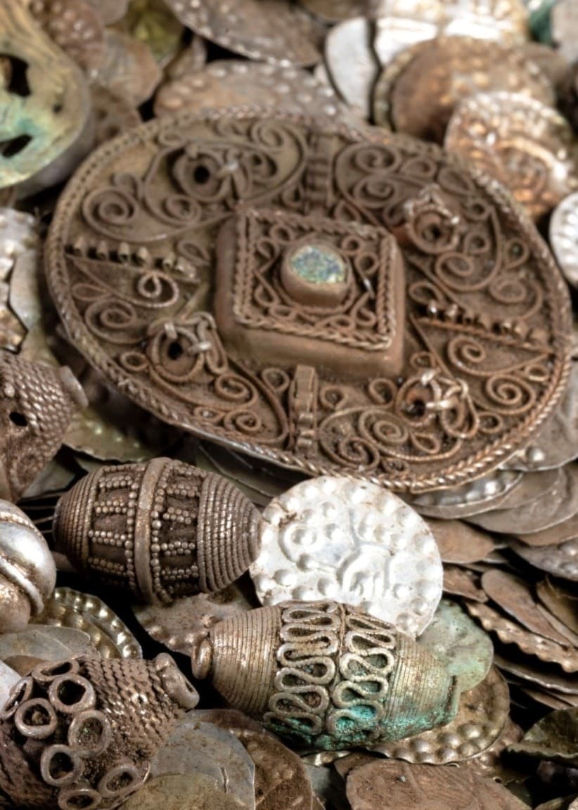 Närbild på en silverskatt med mynt, utsmyckade smycken och ornament i detaljerade mönster, upptäckt i Stockholm. Bilden visar historiska föremål av stort kulturellt värde.