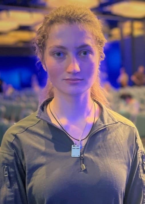 Maria Fartuzhna står i en stor sal med rader av tomma gröna stolar. Hon är på rehabiliteringsresa i Sverige och bär en grå tröja med dragkedja och halsband.