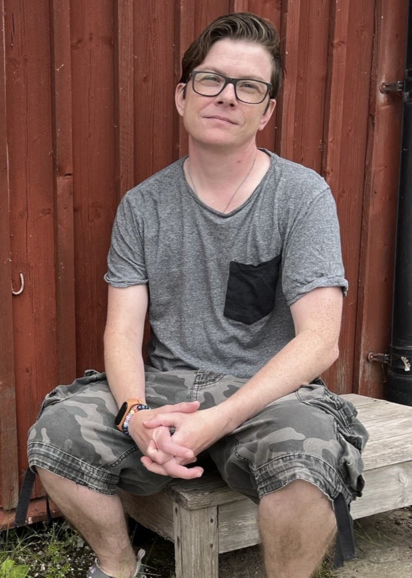 Noah van Dorpel sitter på en låg bänk framför en faluröd husvägg. 
