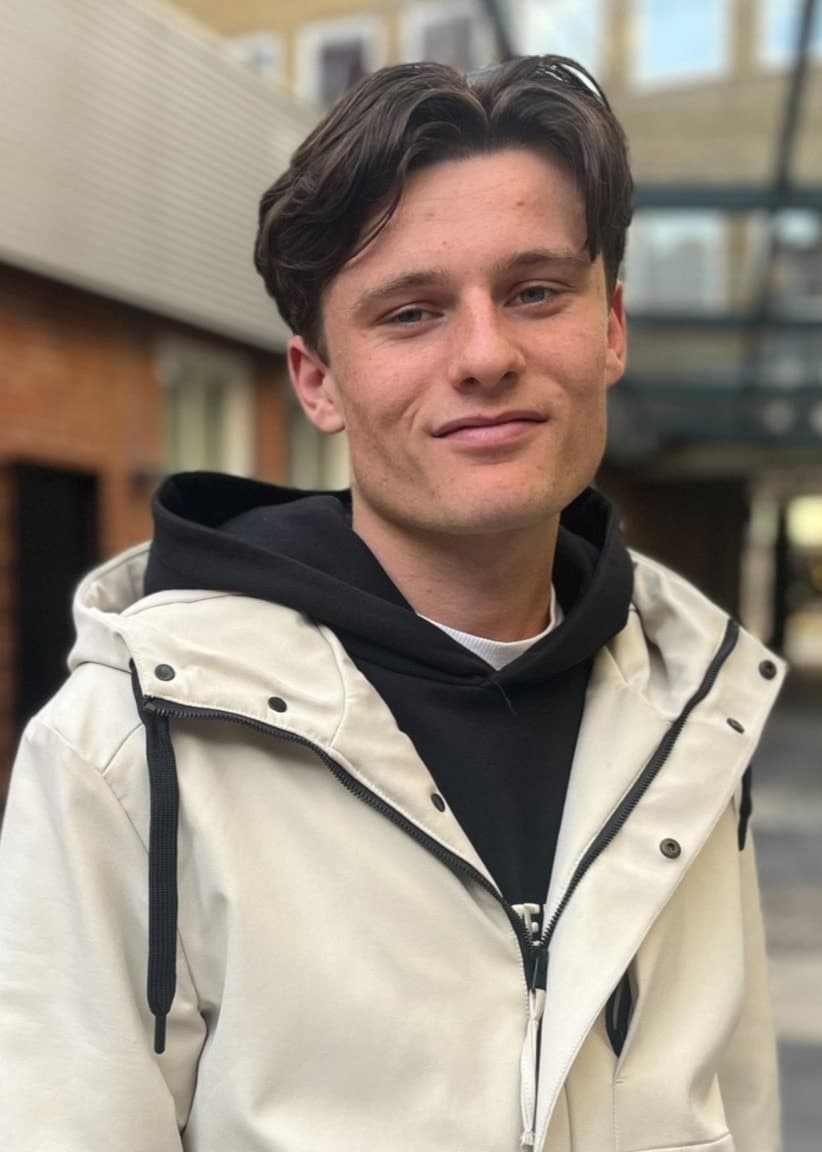 Vilhelm Nordvall, finalist i P4 Nästa Stjärna Malmöhus, står utomhus framför en tegelbyggnad klädd i ljus jacka och svart hoodie.