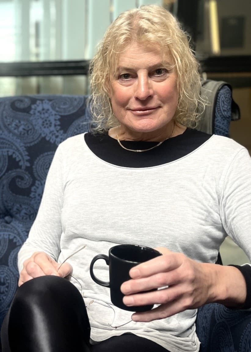 Kim Sandberg, nyhetsprogramledare och nyhetsuppläsare för SVT Dalarna och SVT Gävleborg, sitter avslappnat i en fåtölj med en kaffekopp i handen i en kontorsmiljö.