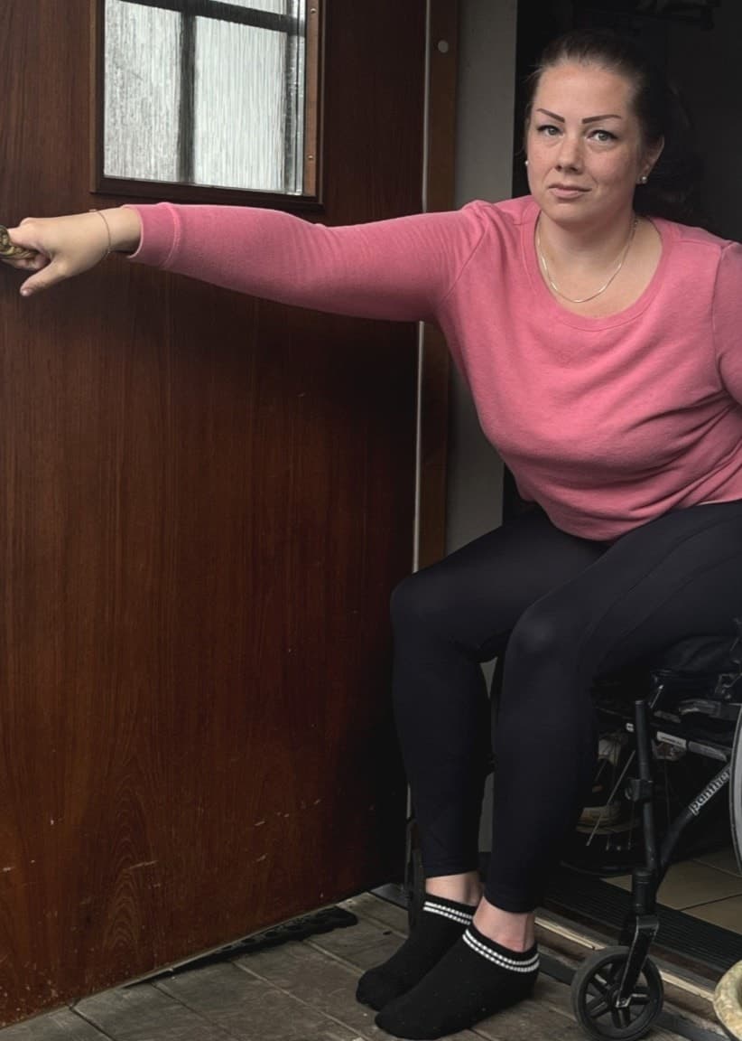 Angelica Henriksen, som använder rullstol, öppnar dörren till sitt vita hus.