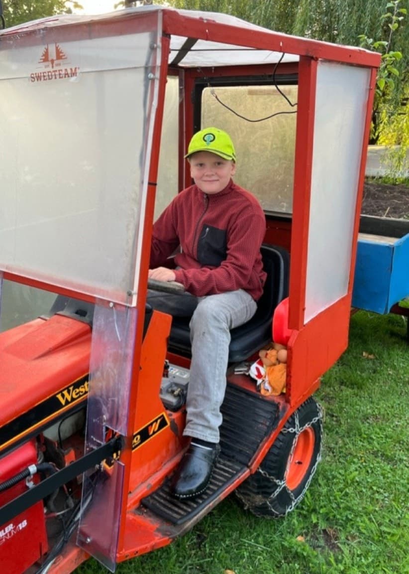 Bildsplitt. Till vänster ett köksbord med pumpor i olika färger och former. Till höger Alfred Sernfalk, 10 år, sitter på en liten traktor med släp. Han har röd flis och en gul keps på sig. Han ler mot kameran.