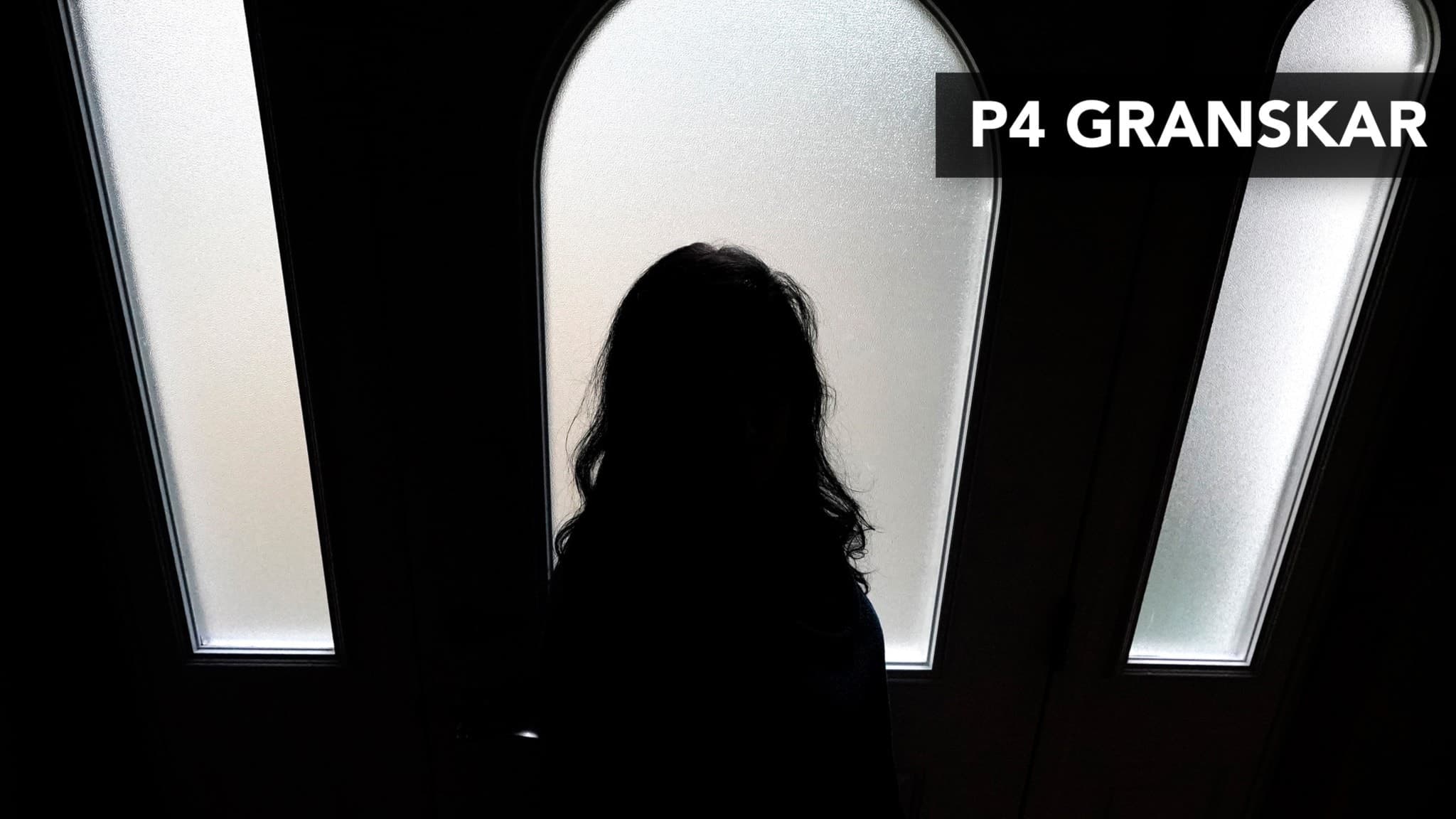 siluett på en kvinna i ett fönster i en trappuppgång i mörker och ljus från fönstren 