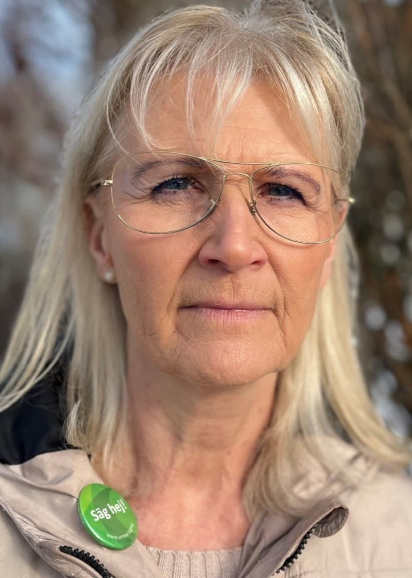 Blond kvinna i vinterjacka står utomhus vid en kal buske.