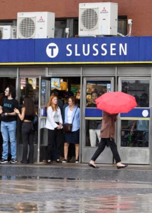 Slussens tunnelbanestation i Stockholm med människor under paraplyer.