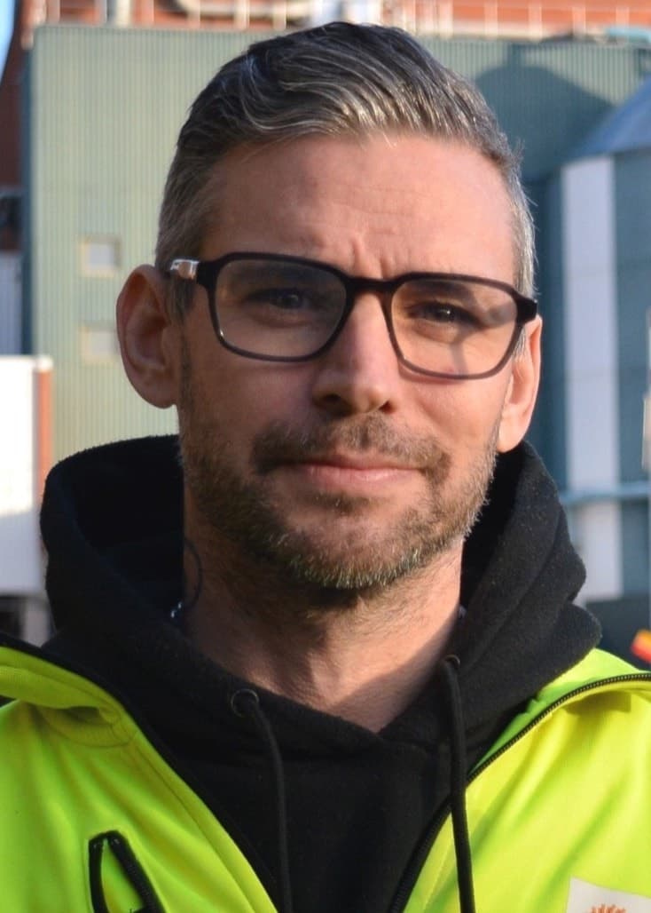 Andreas Karlsson står med glasögon och i en gul skyddsjacka framför Stora Ensos fabrik i Skutskär. Han tittar in i kameran. 