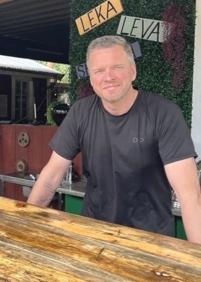 Richard Näslin står vid en rustik trädisk på en servering utomhus. Han driver campingen Gunnagård i Ullared.