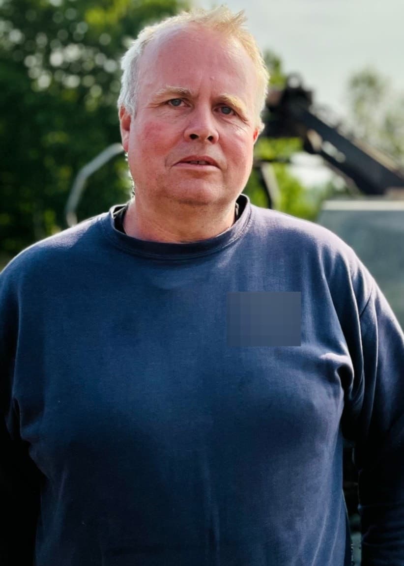 Markus Andersson står framför en brandskadad maskin på ett fält, omgiven av grönska och en ljus himmel. Händelsen inträffade under hans arbete när maskinen började brinna.