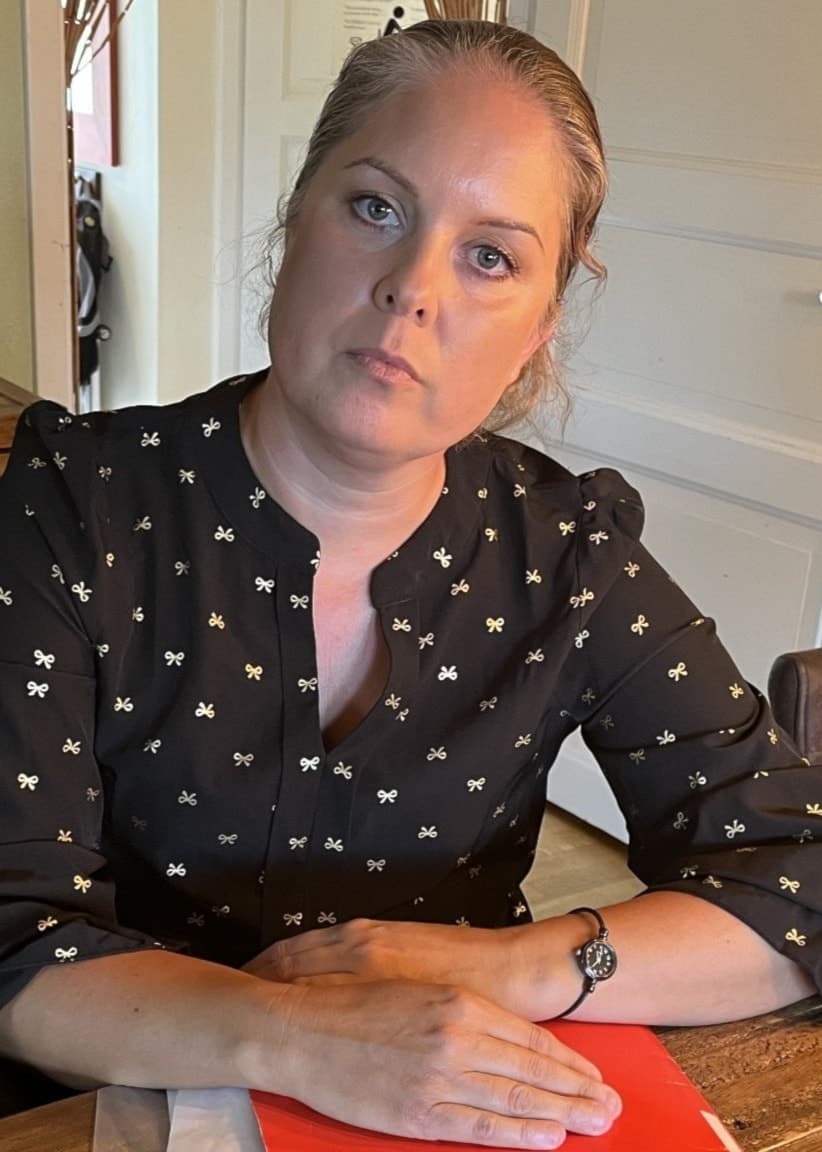 Petra Åslund sitter vid ett bord med en röd mapp full av papper framför sig.
