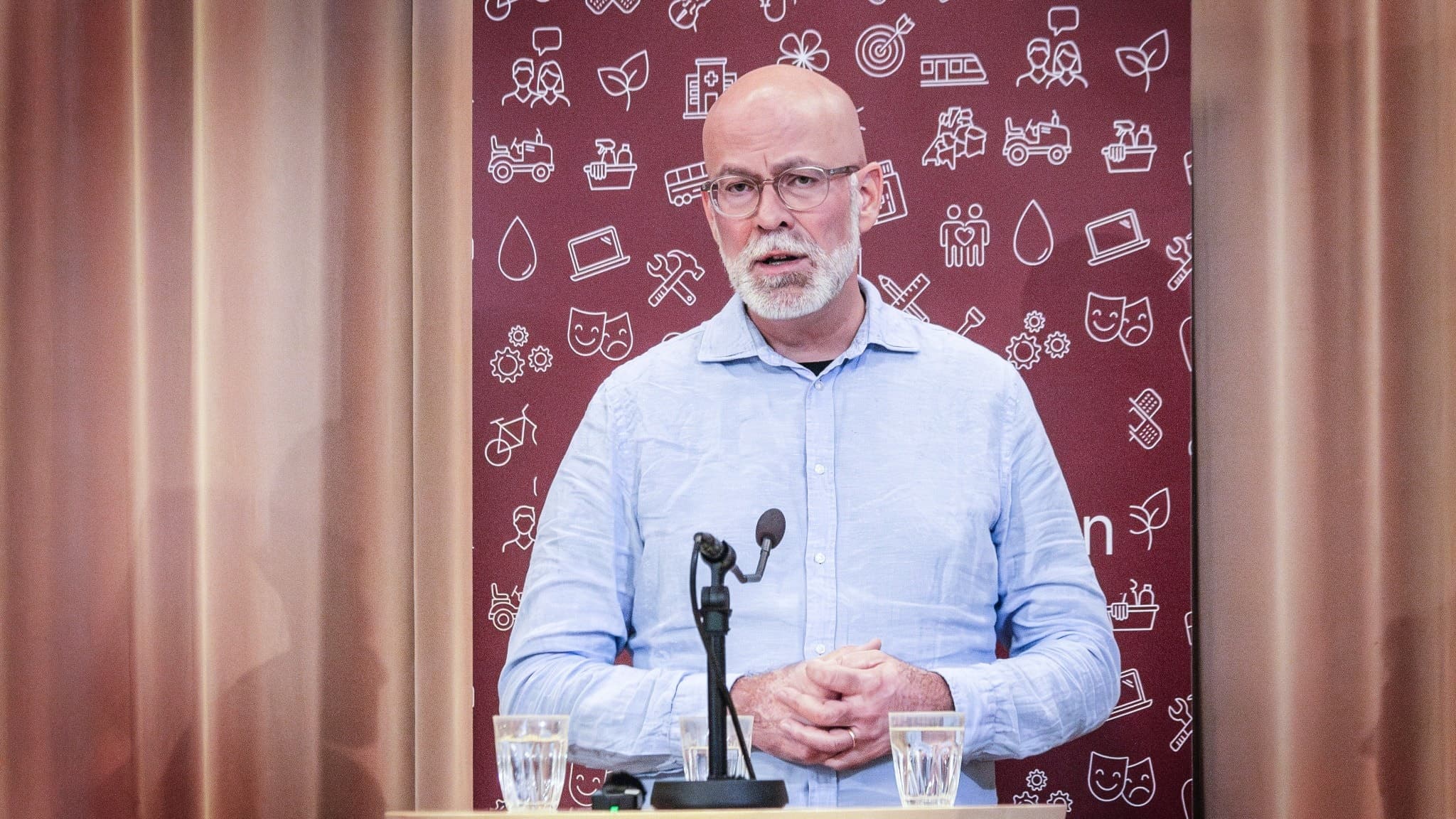 Barnklinikens verksamhetschef Simon Rundquist under en presskonferens framför ett bord med vattenglas och en mikrofon