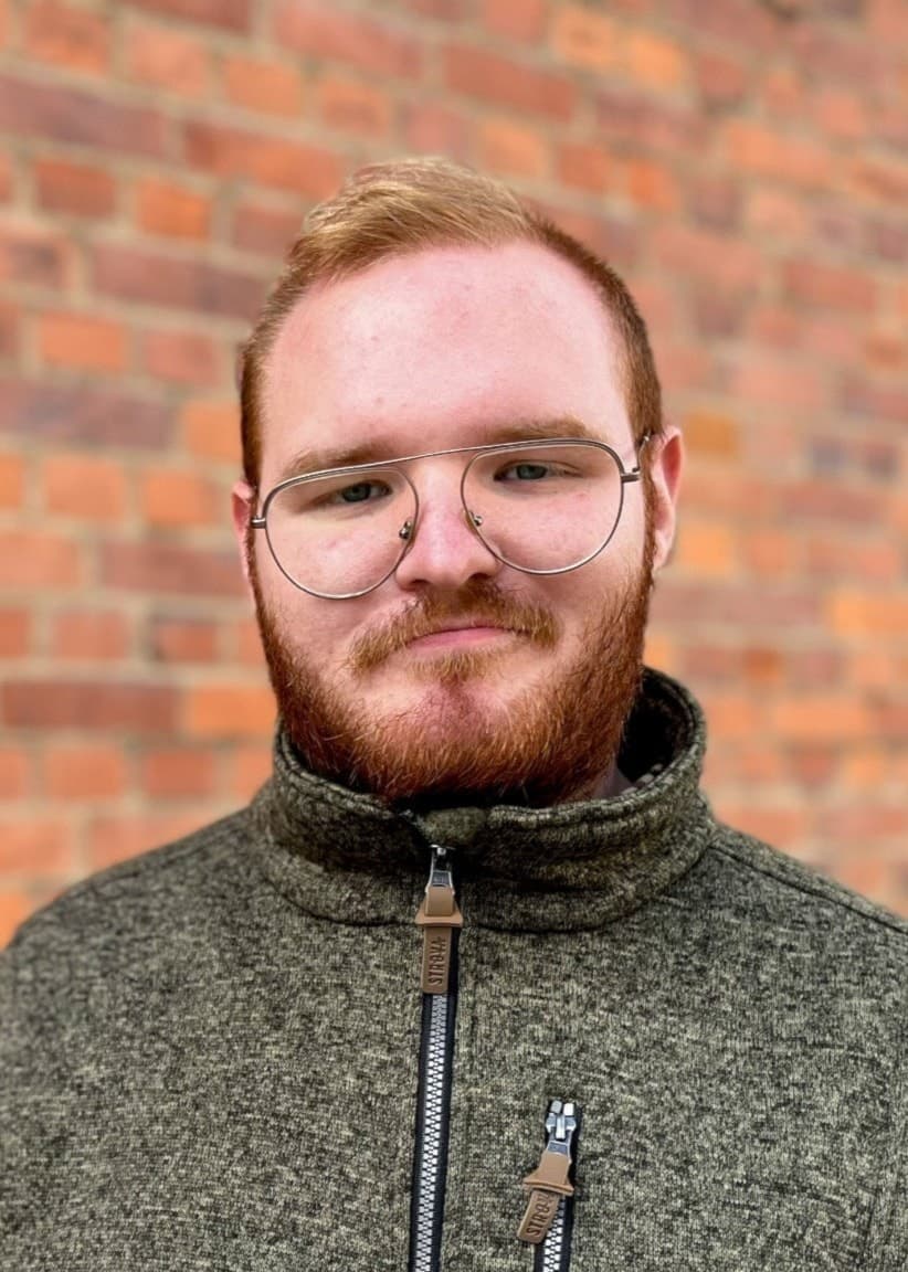 Simon Lixenstrand står framför en tegelvägg, klädd i en grå ulltröja med dragkedja.