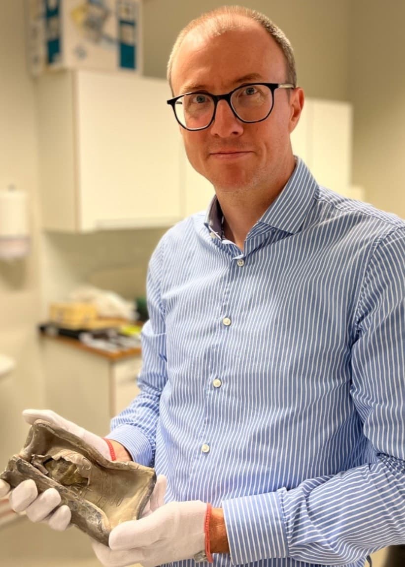 Johannes Daun, enhetschef på Textilmuseet och Borås museum, håller i en blyask med vita handskar. Bredvid visas en glasflaska med ett brev inuti, placerad på en vit duk.