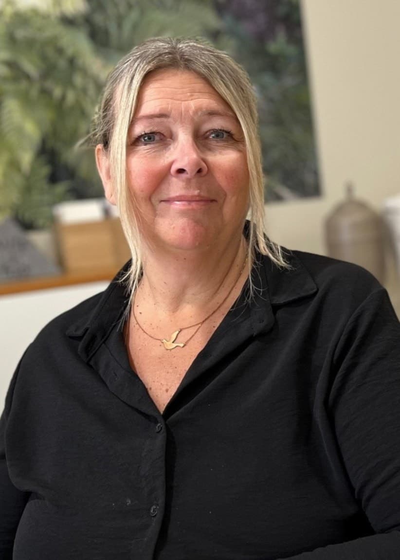 Katrin Grönlund, borgerlig officiant på begravningsbyrån Fonus i Luleå, sitter vid ett bord i ett ljust rum med gröna växter och urnor i bakgrunden.