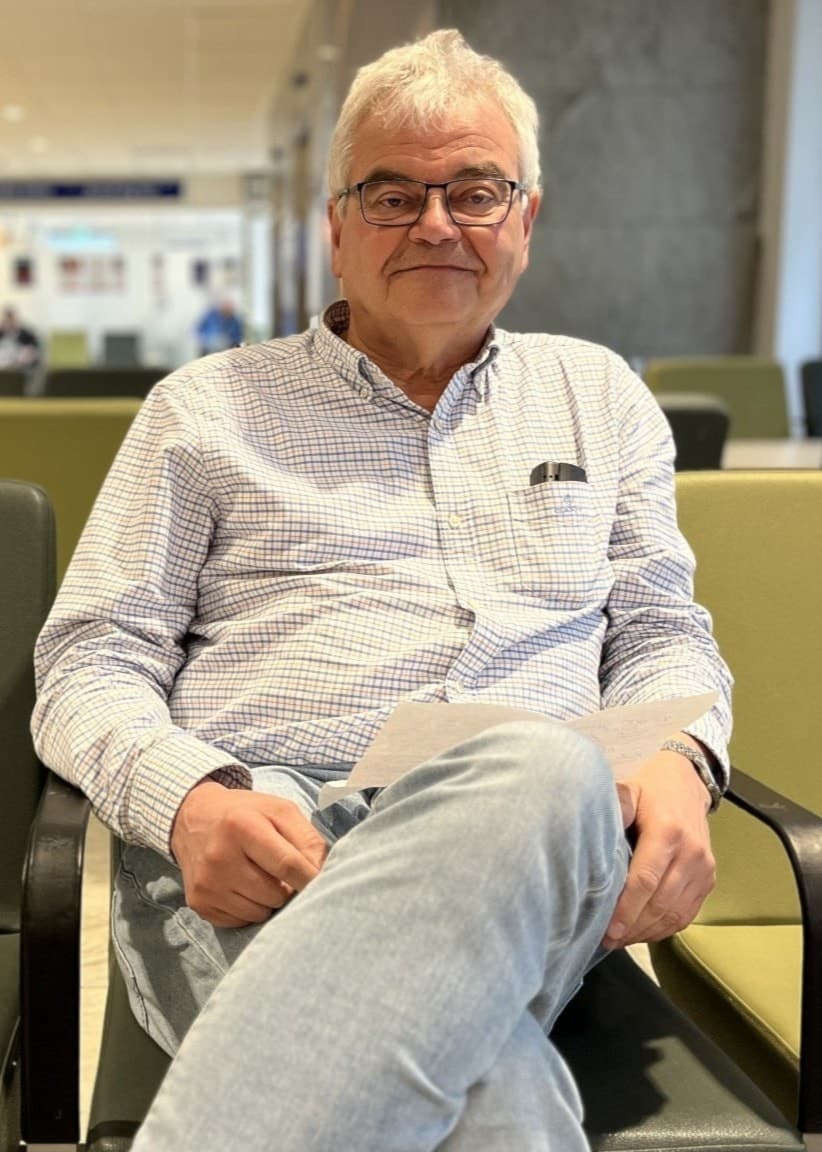 En man, identifierad som Stefan Söderberg, sitter avslappnat på en stol i ett modernt väntrum. Han bär en vit skjorta med mönster och ljusblå jeans. Bakgrunden visar personer i rörelse.