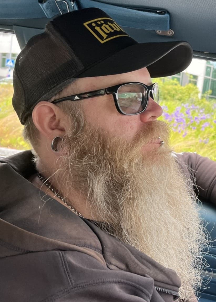 Robin Sjöbom sitter vid ratten i en Chevrolet Bel Air från 1968 under Summer Meet. Han bär keps och hoodie, och bilens blå interiör samt grönskande omgivning syns i bakgrunden.