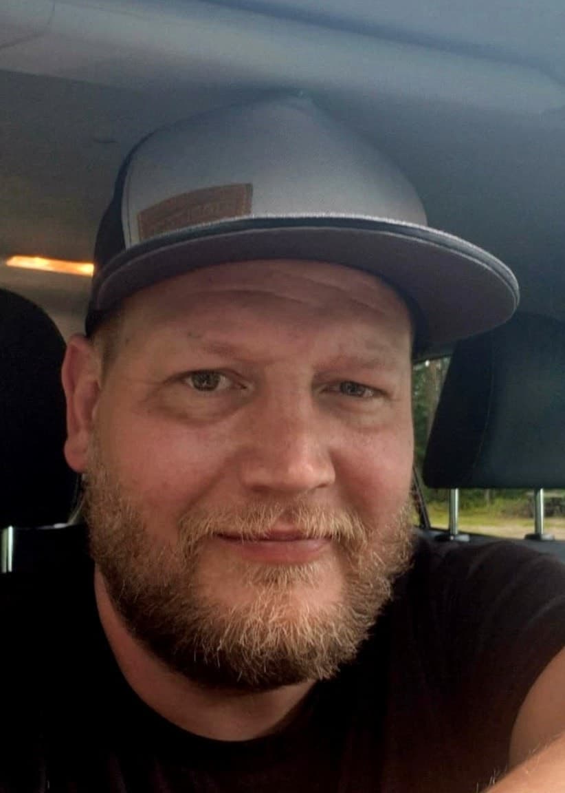 En med keps i en bil till vänster, till höger trafik på en väg.