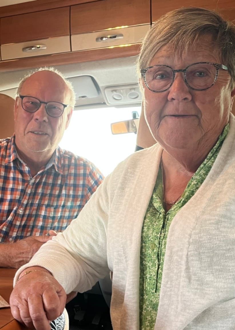 Maria och Håkan Bäckman sitter i sin husbil, besvikna över begränsningar för husbilsparkering. Till vänster syns en skylt med förbud mot camping och husbilar.