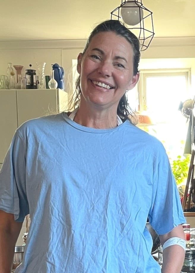 En kvinna i blå tshirt och beiga byxor står i ett kök.