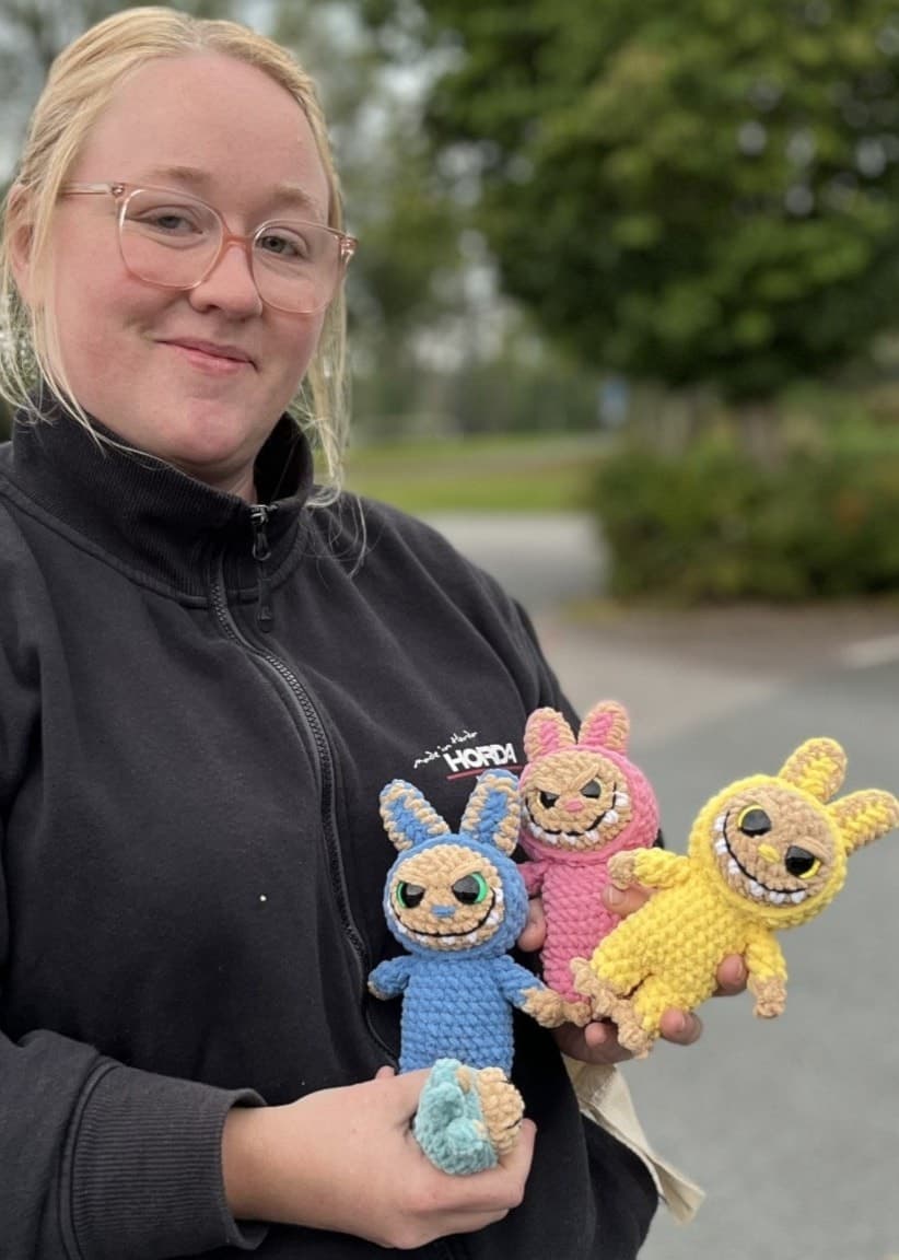 Emma Petersson från Horda utanför Värnamo visar upp tre färgglada, egenvirkade monsterdockor utomhus på en parkeringsplats.
