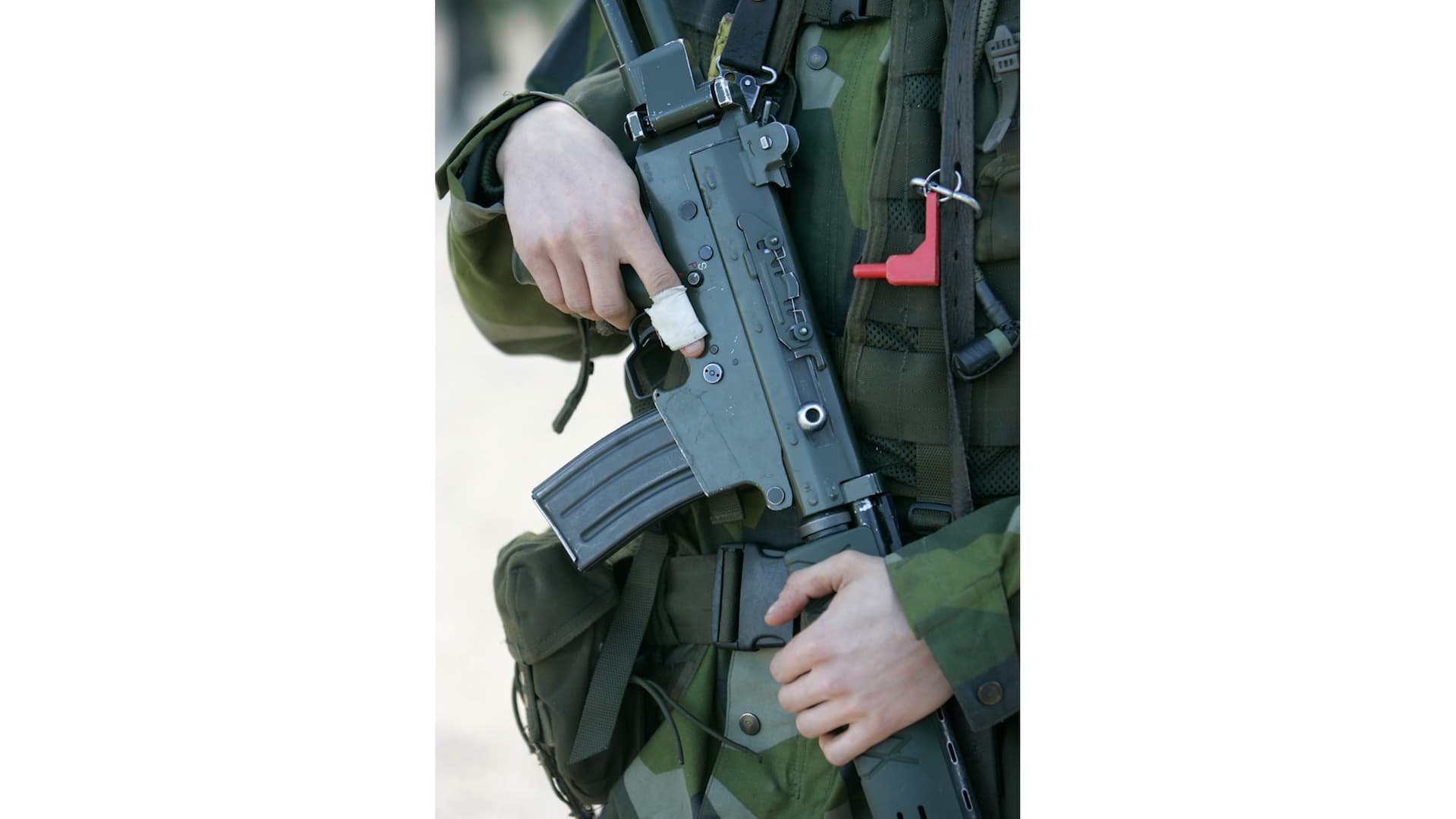 Svenska soldater i kamouflageuniformer deltar i en militärövning i Stockholm. Den svenska flaggan syns på en soldats arm, medan gevär och andra soldater skymtas i bakgrunden.