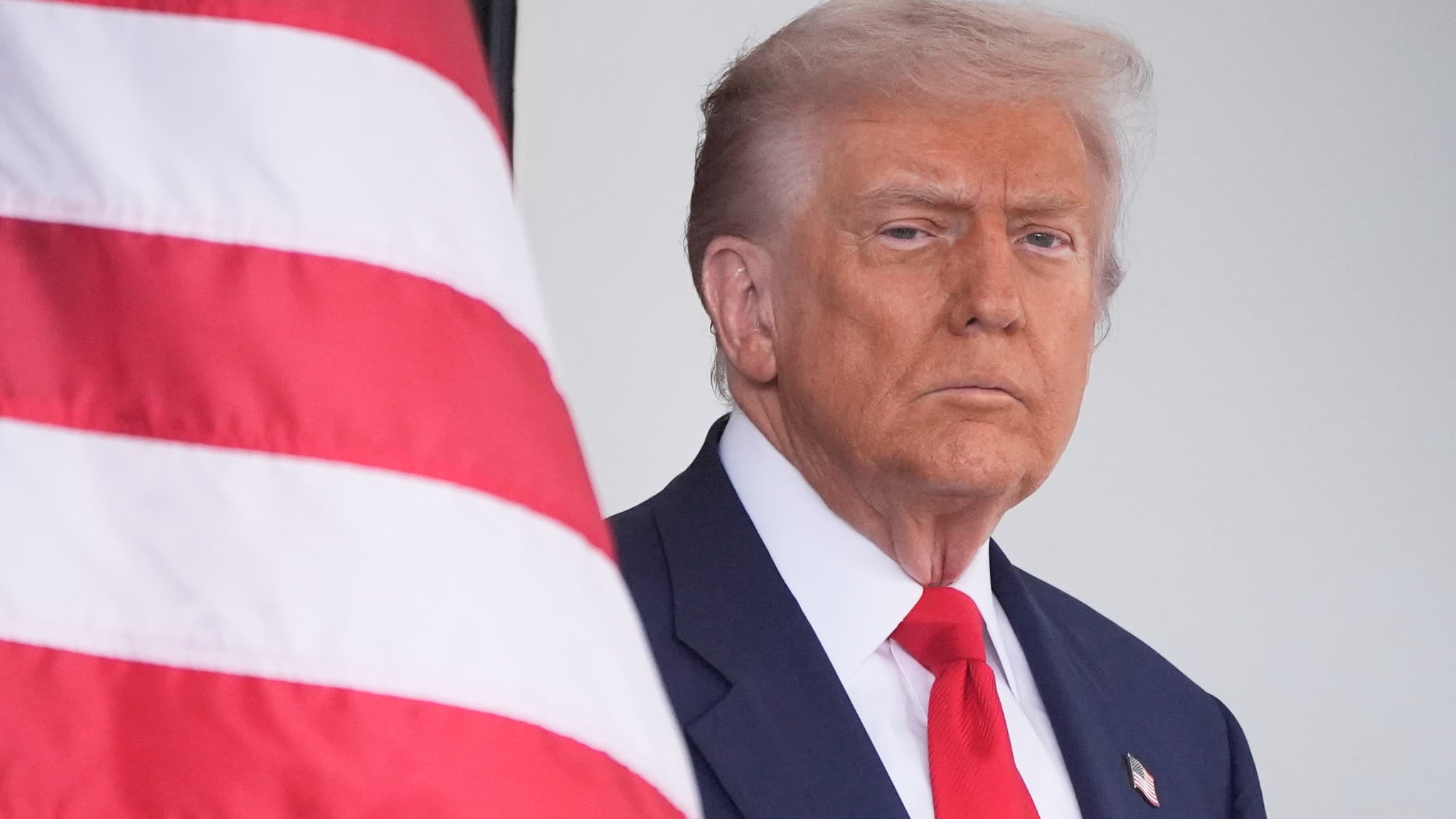 USAs president Donald Trump ser allvarlig ut i blå kostym och klarröd slips. Till vänster skymtar delar av en amerikansk flagga. Foto: Mark Schiefelbein / AFP