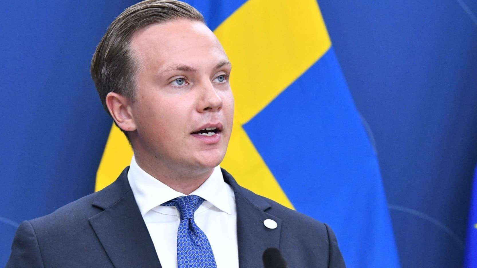 Man med bakåtslickat hår gestikulerar vid en presskonferens.