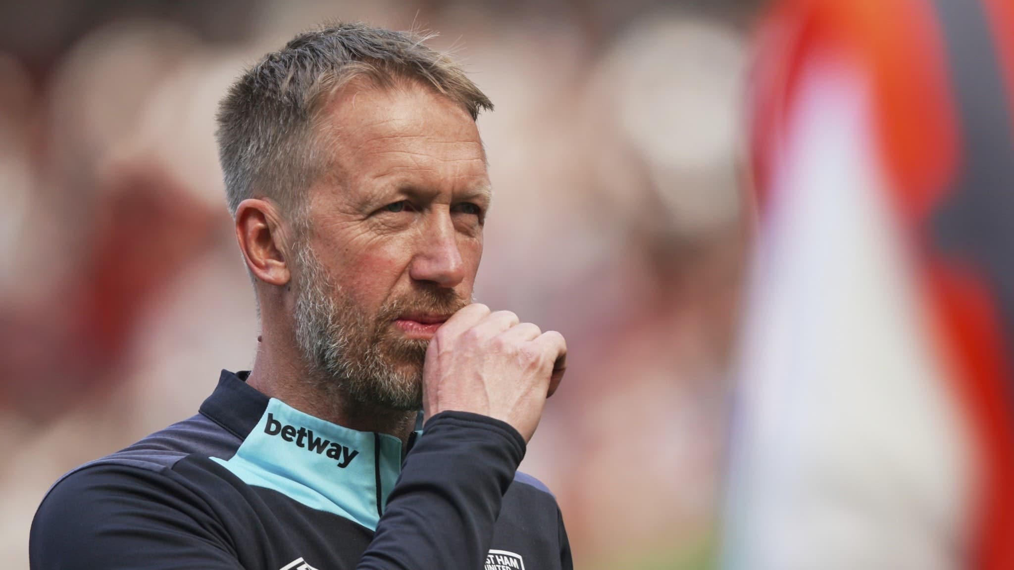 West Hams tränare Graham Potter står på planen i träningskläder med klubbens emblem synligt, mot en bakgrund av publikhav och flaggor på Old Trafford under Premier League-matchen.