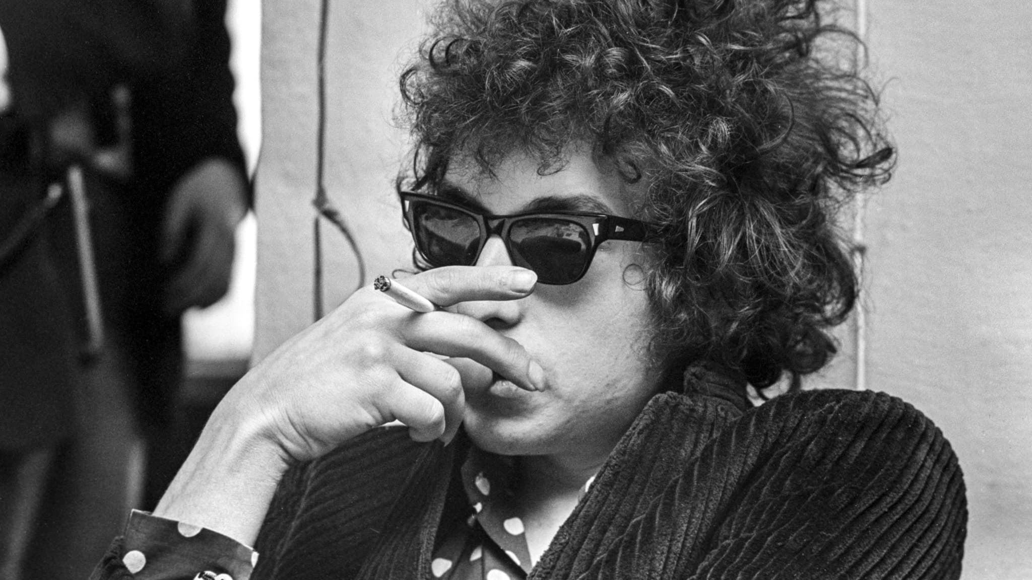 Bob Dylan med solglasögon på sig och en cigarett i handen vid en presskonferens i Solna 28:e april 1966,